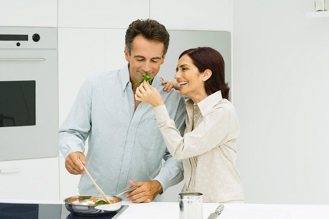 Man cooking, woman holding up basil for man to smell