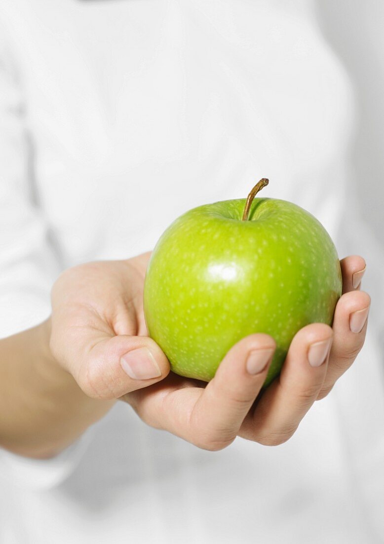 Frauenhand hält einen grünen Apfel