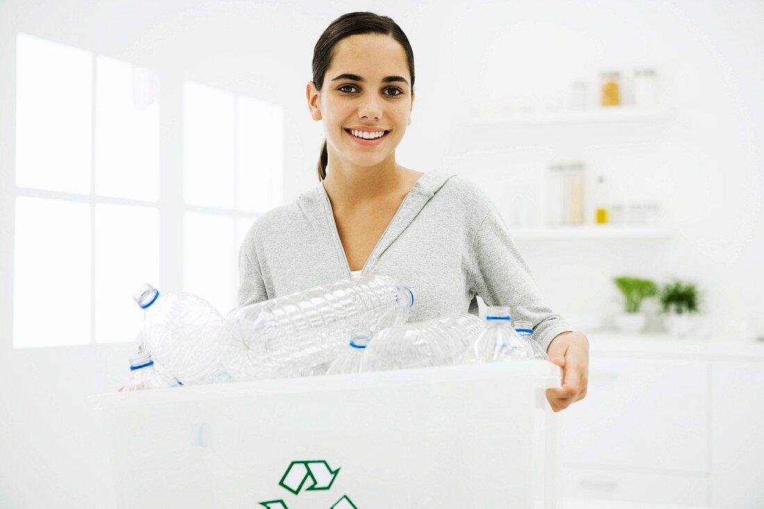 Teen girl carrying recycling bin full of plastic bottles, smiling at camera