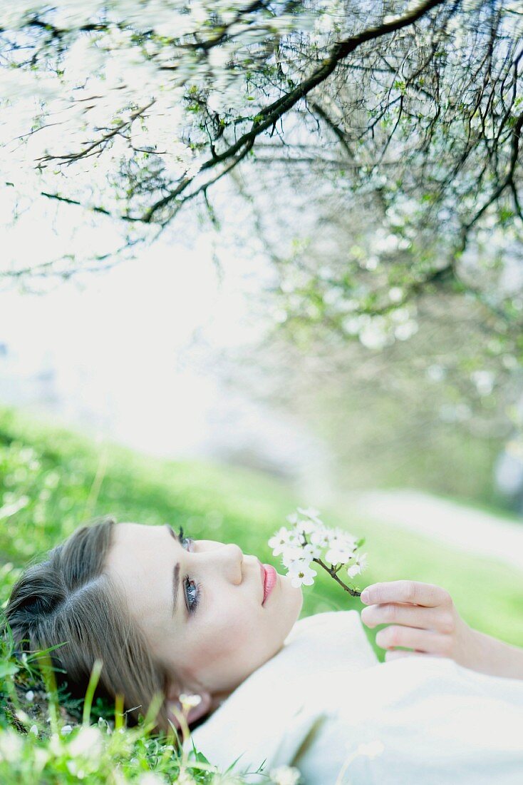 Teenage girl lying on the ground, smelling flower, looking up