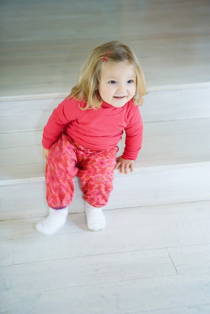 Blonde toddler girl sitting on steps, smiling