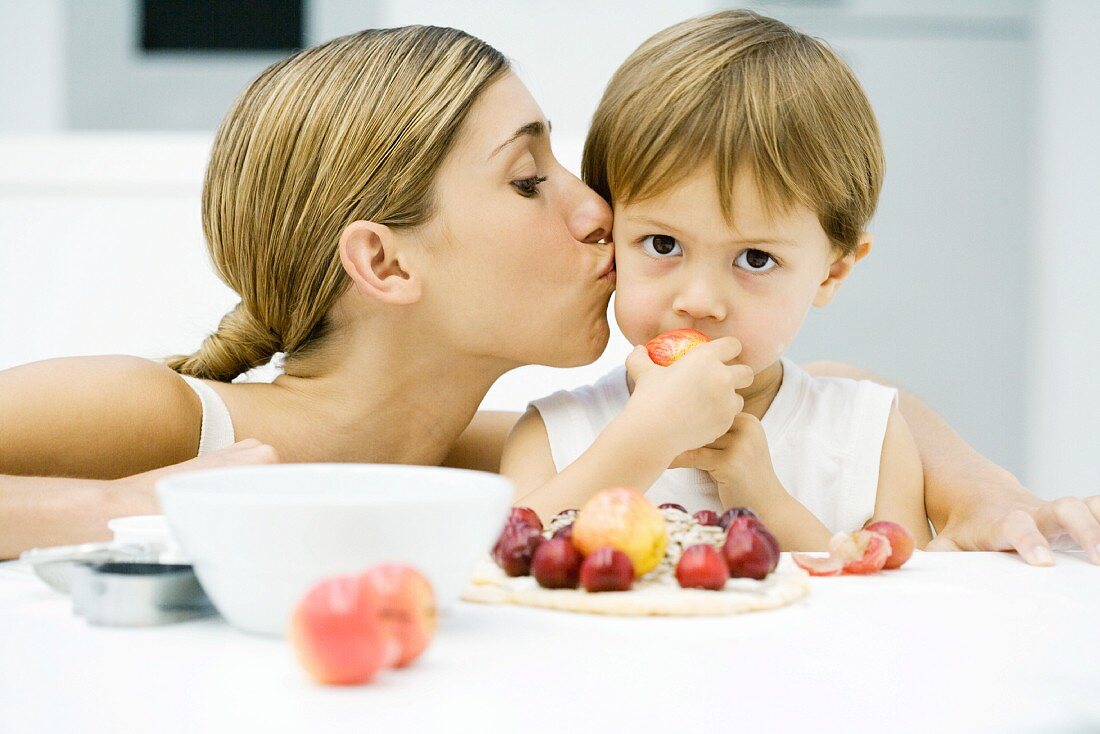 Woman kissing little boy on cheek, boy eating apple