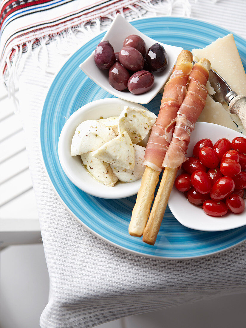 A plate of starters with olives, cheese, mozzarella, tomatoes and grissini