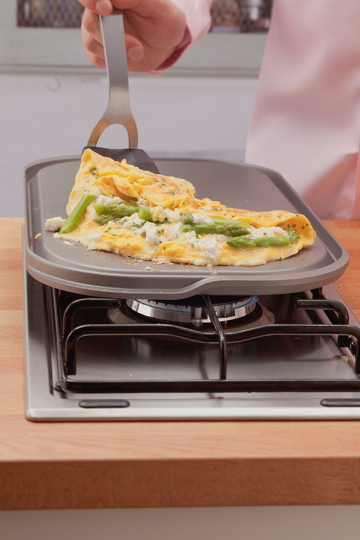 A green asparagus and feta omelette being made on a hot stone