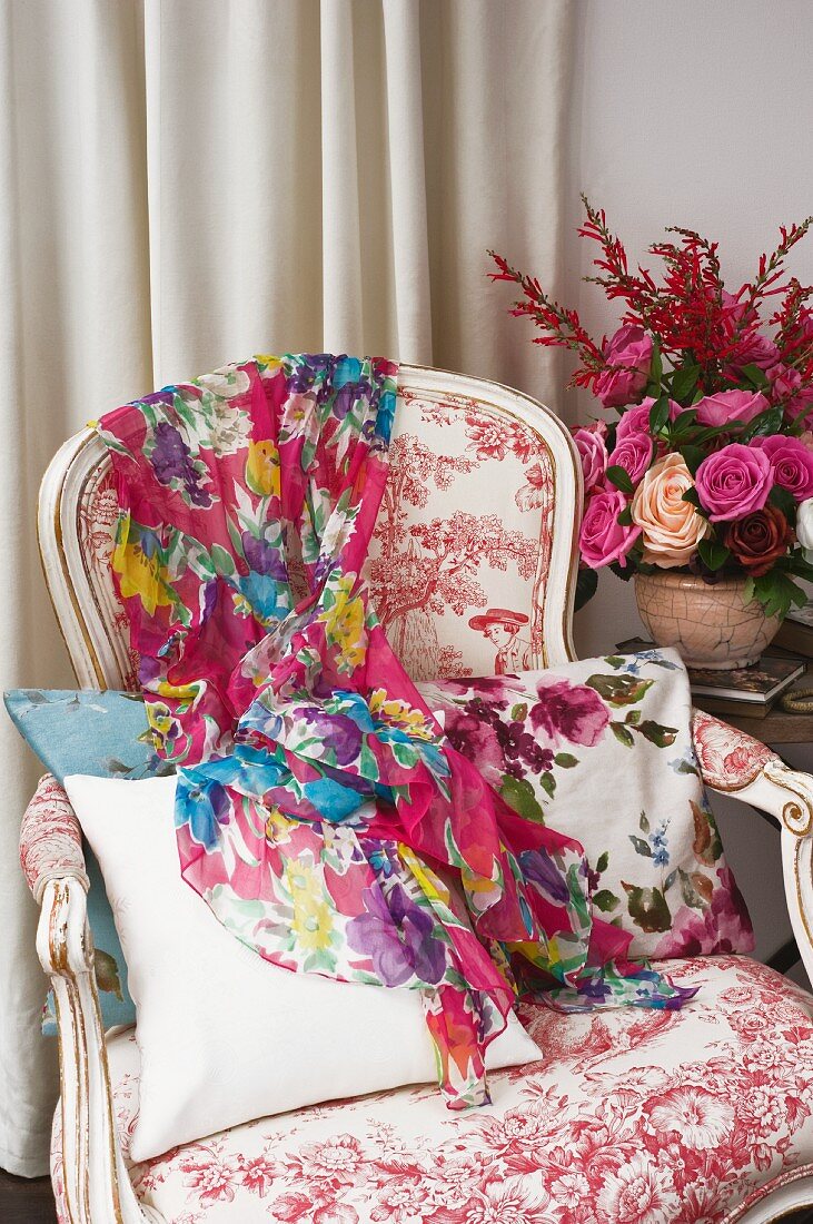 Buntes Tuch auf Sessel im Rokokostil neben Blumengesteck