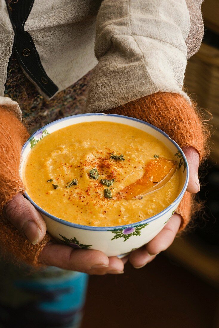 Frau hält Schale mit Butternusskürbis-Kokos-Suppe