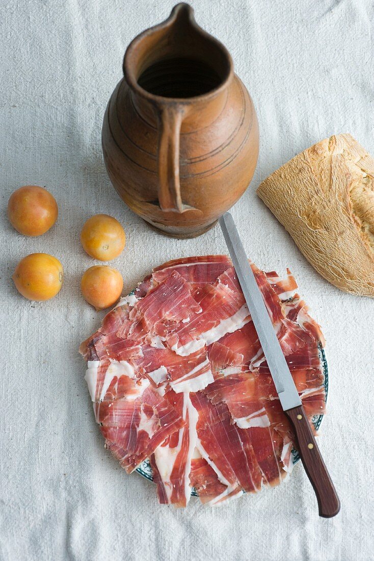 Sliced Prosciutto, plum tomatoes, white bread and a terracotta jug