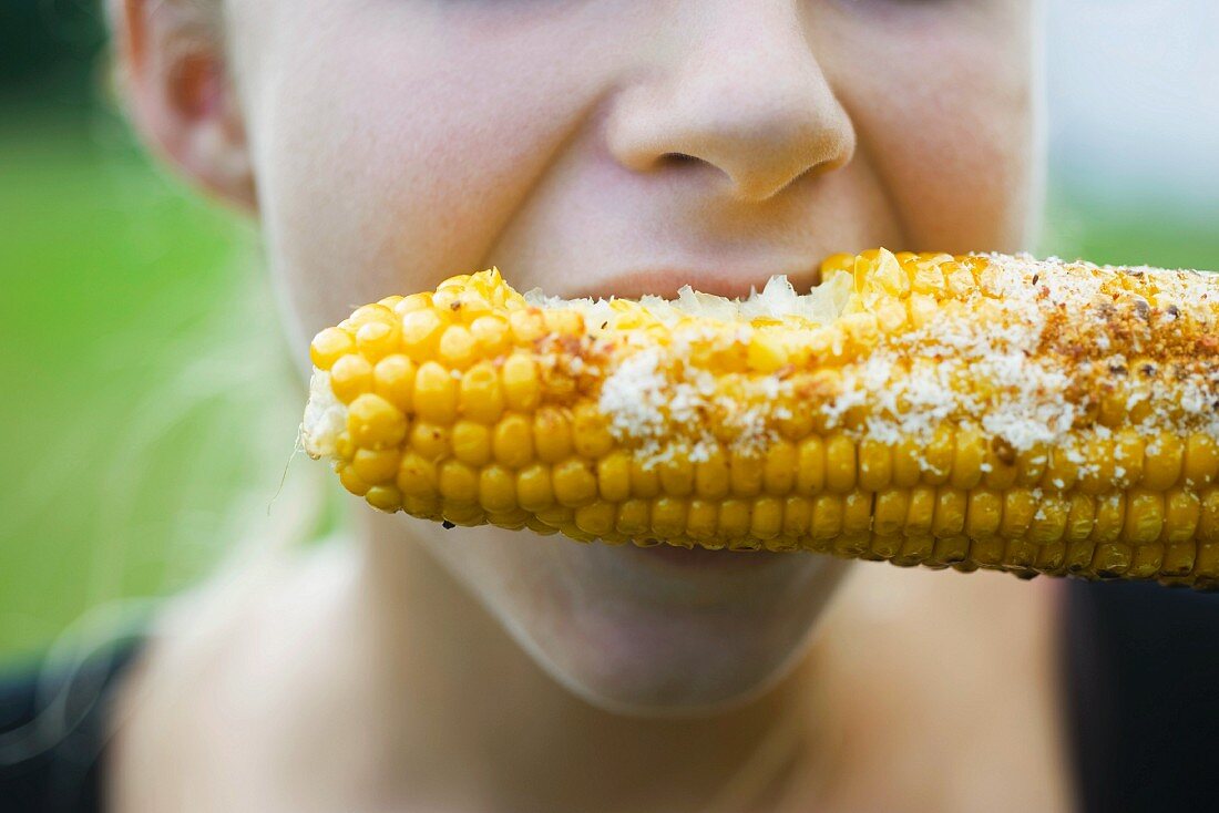 A person eating grilled corn cob