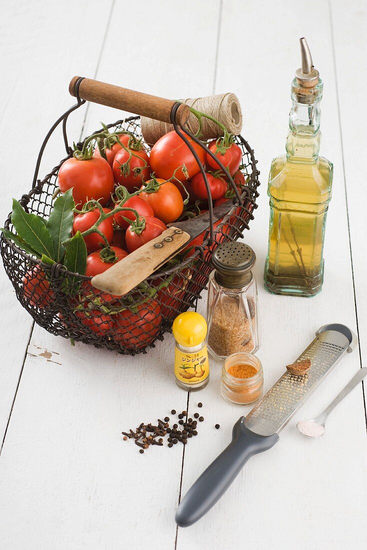 Frische Tomaten in einem Drahtkorb, Olivenöl und Gewürze