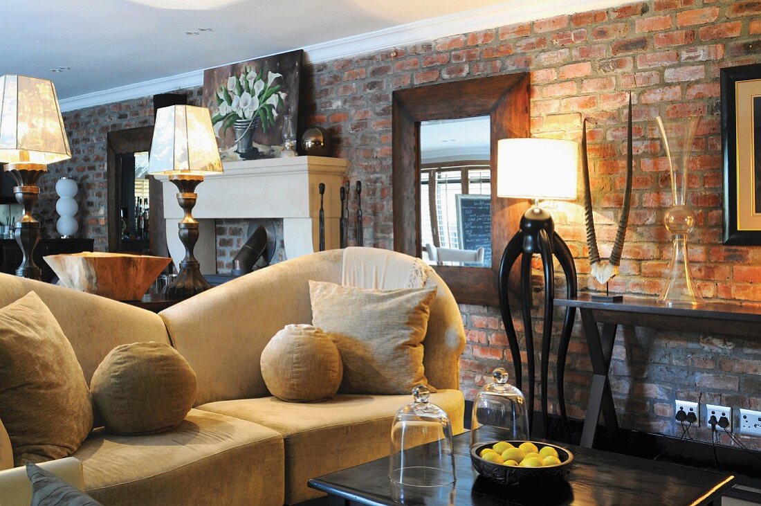 Interior with beige sofa, warm lighting provided by standard lamps, exposed brick wall and African decor