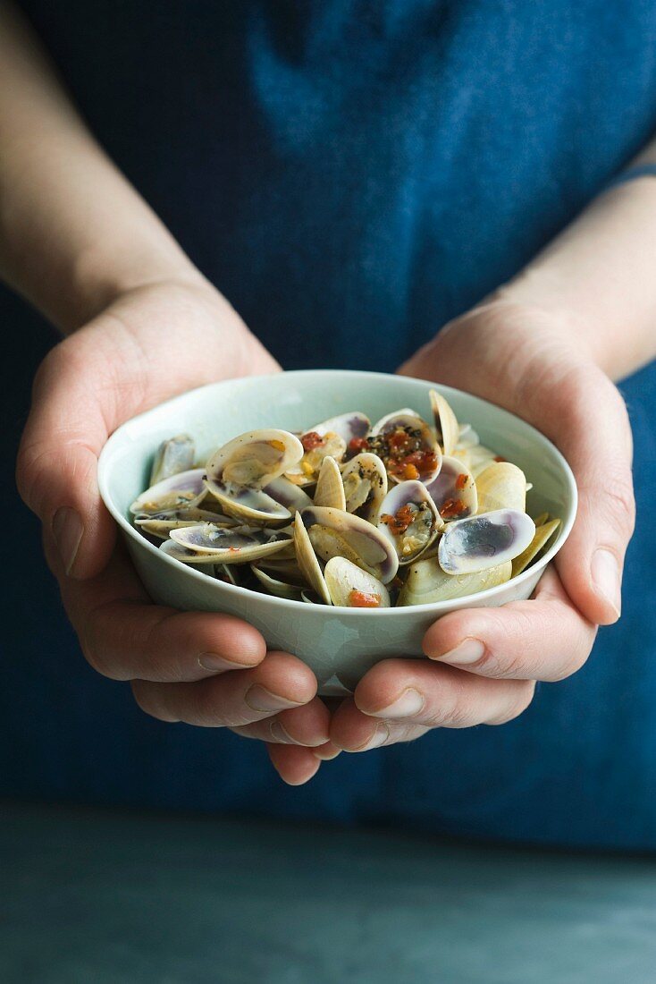 A person holding a bowl of Venus clams with limes and chilli paste