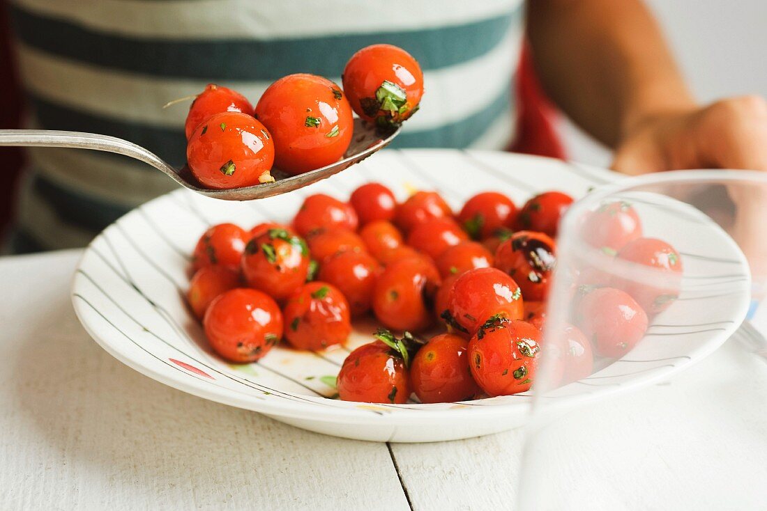 A person eating cherry tomato confit with herbs