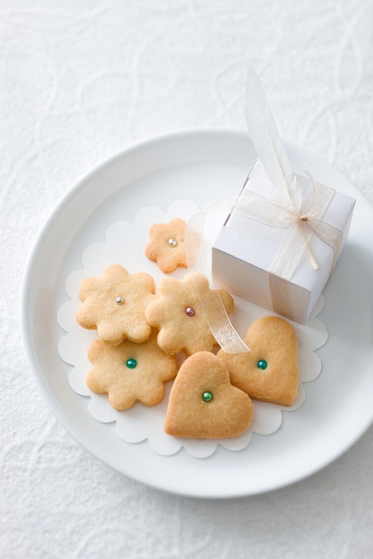 Heart and flower-shaped biscuits decorated with sugar pearls and a small gift on a plate