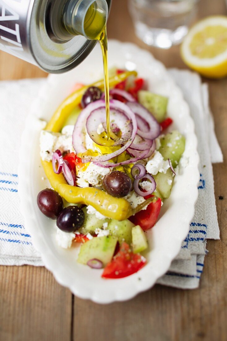 A Greek salad being drizzled with olive oil