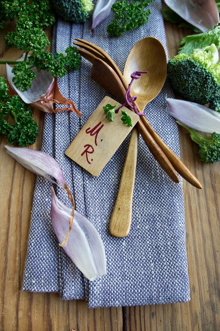Wooden cutlery with a name label on a napkin between shallots and broccoli