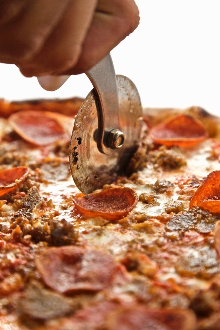 Hand Using a Pizza Wheel to Cut a Pepperoni and Sausage Pizza