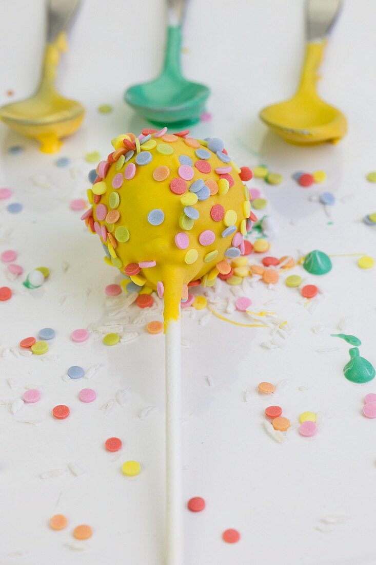A yellow cake pop decorated with colourful sugar sprinkles
