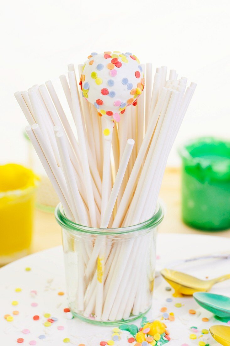 A white cake pop and lots of lolly sticks in a glass