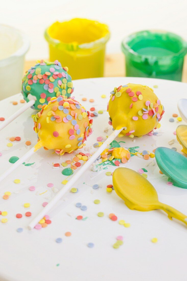 Cake pops decorated with colourful sugar sprinkles and icing sugar on spoons