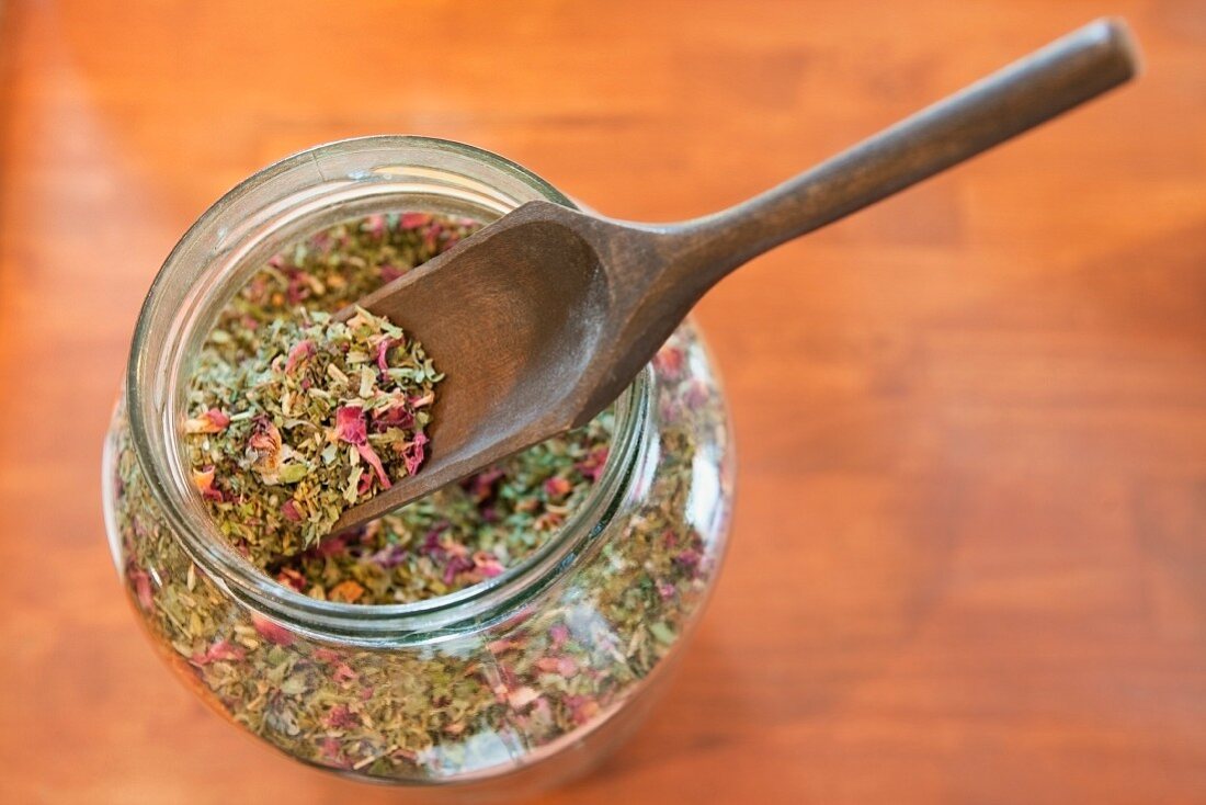 Dried herbs and flowers in a jar with a wooden scoop