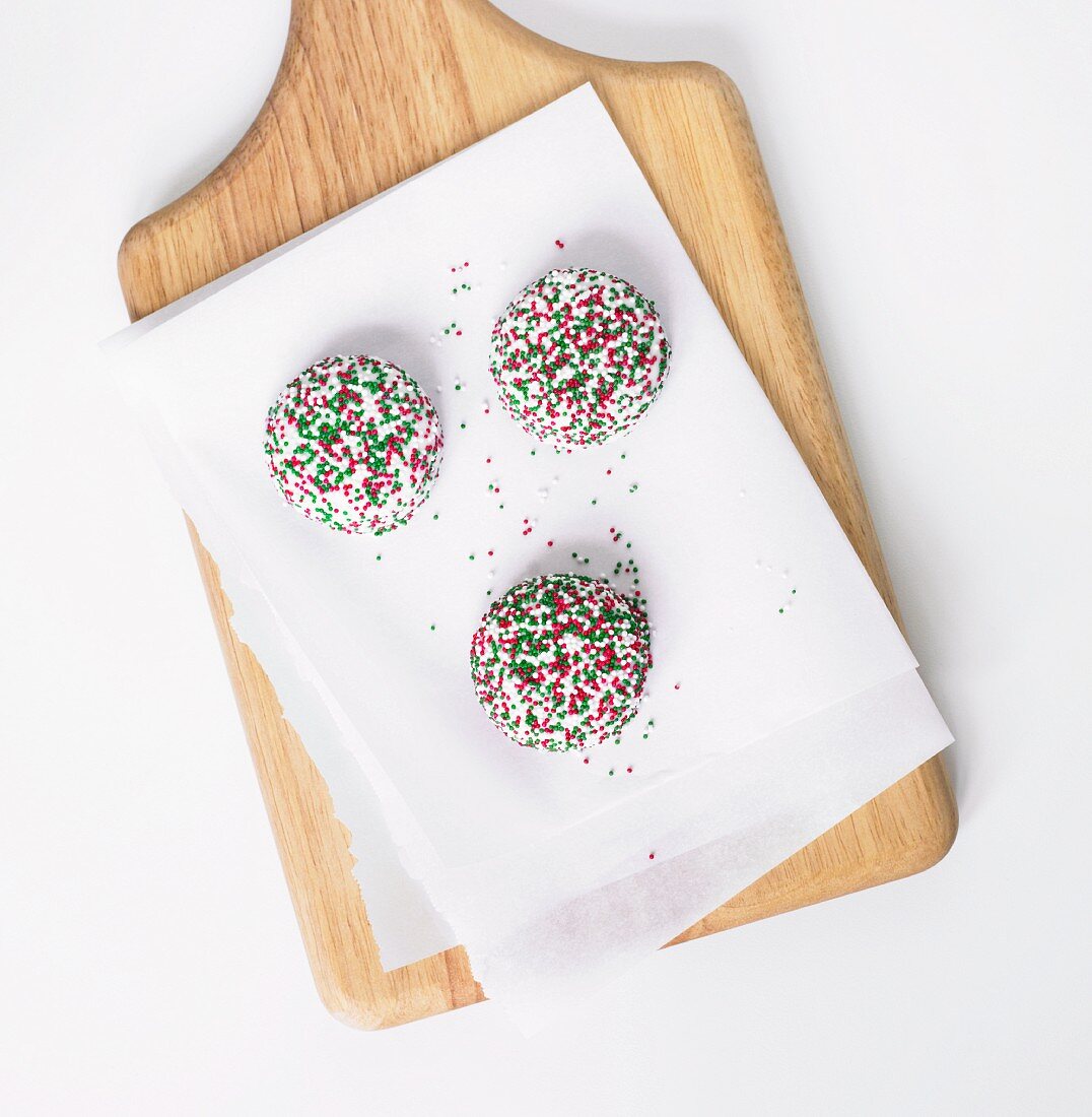 Three Vanilla Cookies with Christmas Colored Sprinkles; On Parchment on Cutting Board