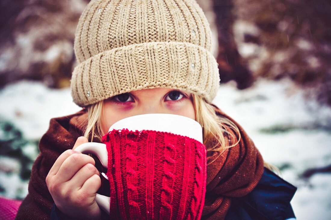 Kleines Mädchen trinkt eine Tasse Tee im Winter