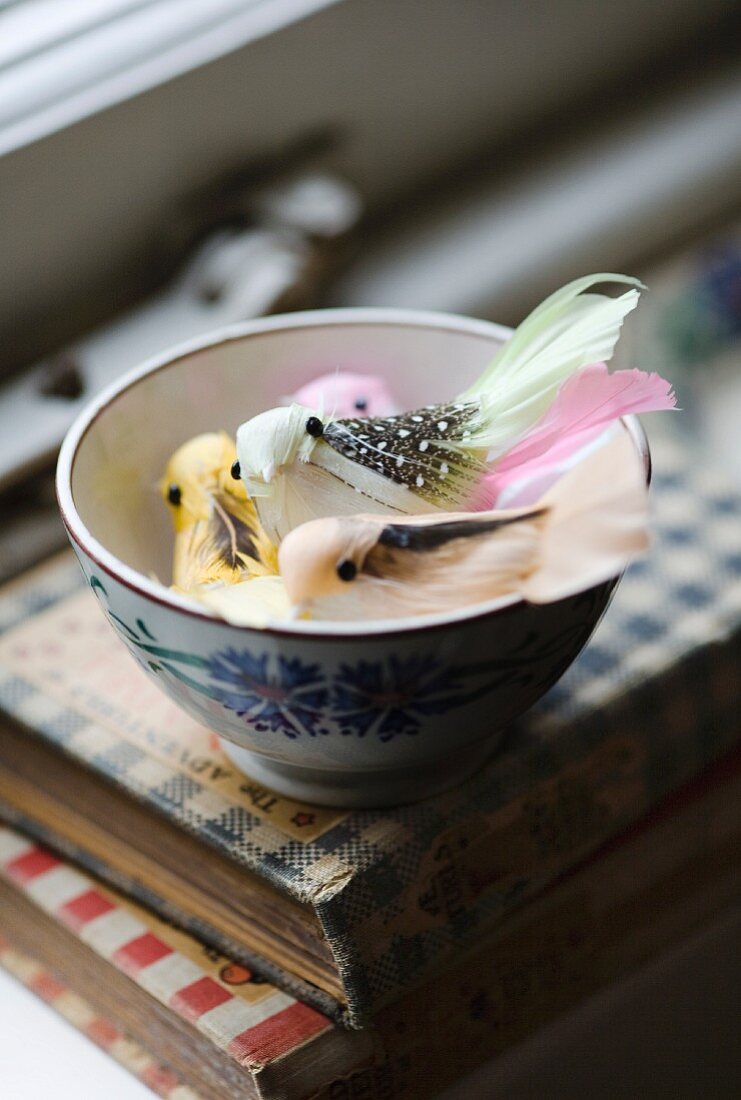 Pastel coloured decorative birds in a bowl on a stack of books