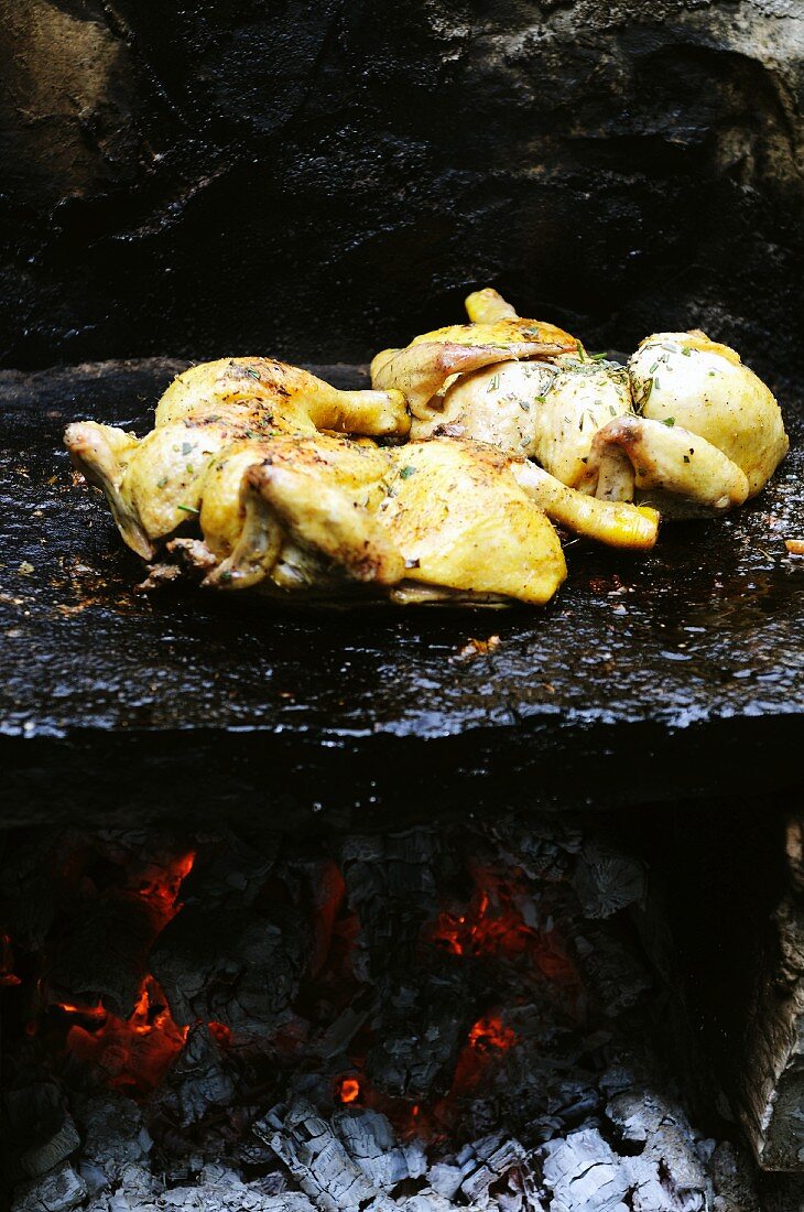 Spatch-cock chickens cooking on a granite stone over fire