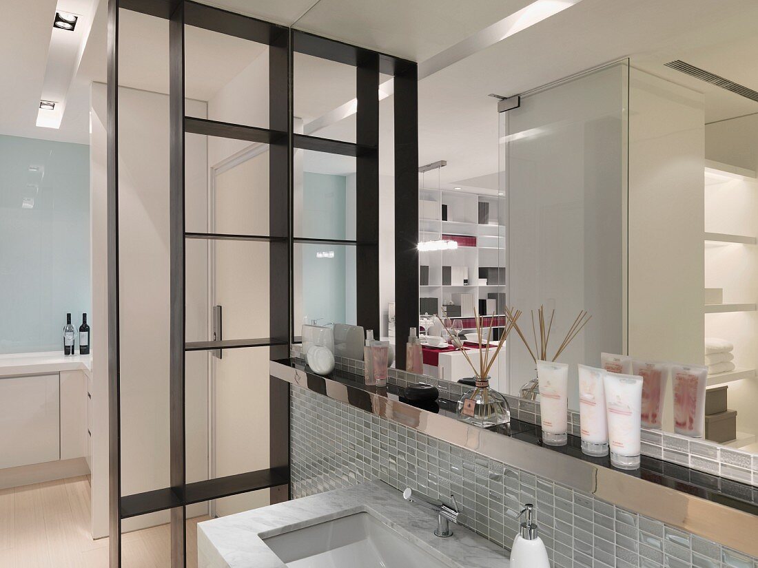 Ausschnitt eines modernen Waschtisches mit Wandspiegel neben Raumteiler aus schwarz lackiertem Metall