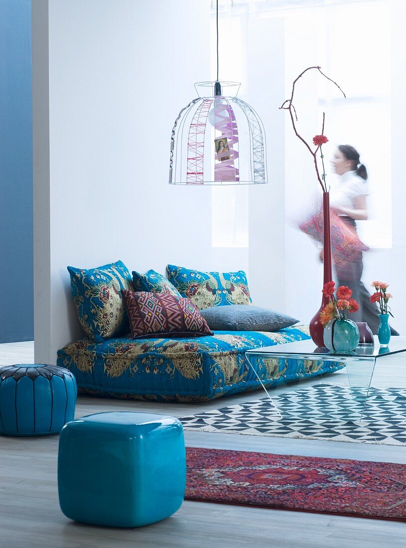 Couch with Oriental upholstery and scatter cushions, wire frame lampshade and stools in living room