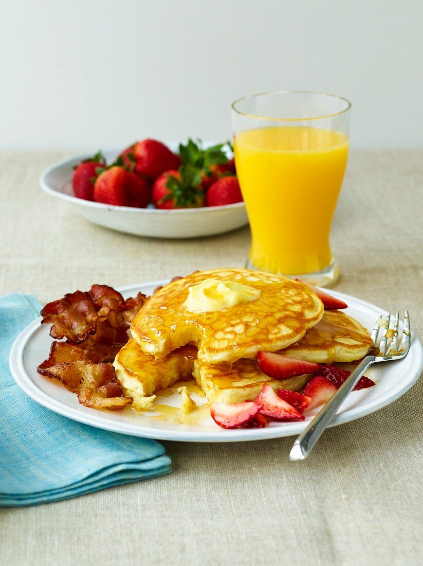 Pancakes mit Butter und Ahornsirup, Bacon und Erdbeeren, Orangensaft (USA)