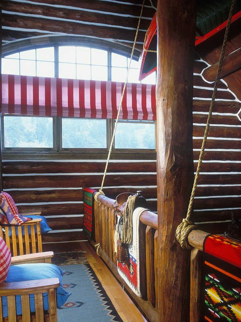 View from log cabin gallery to large, semicircular window; Native American woven rugs on balustrade, canoe hanging from ceiling