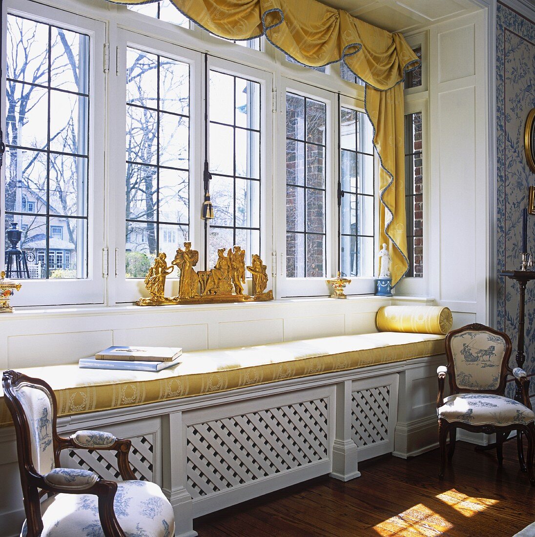 Large window in country house with golden yellow cushions on window seat and gilt ornaments on windowsill