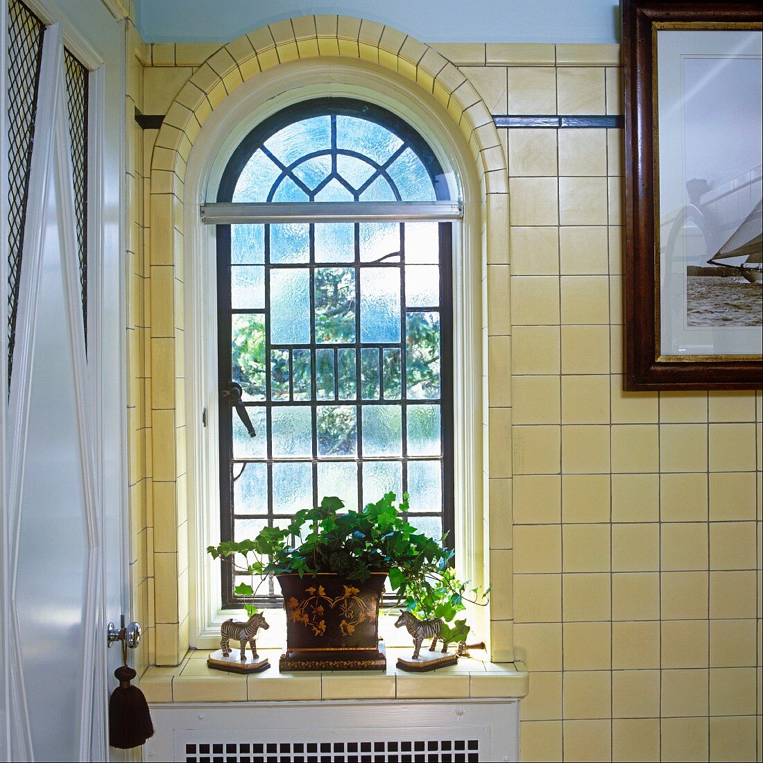 Leaded glass window with rounded arch, potted geranium and horse figurines
