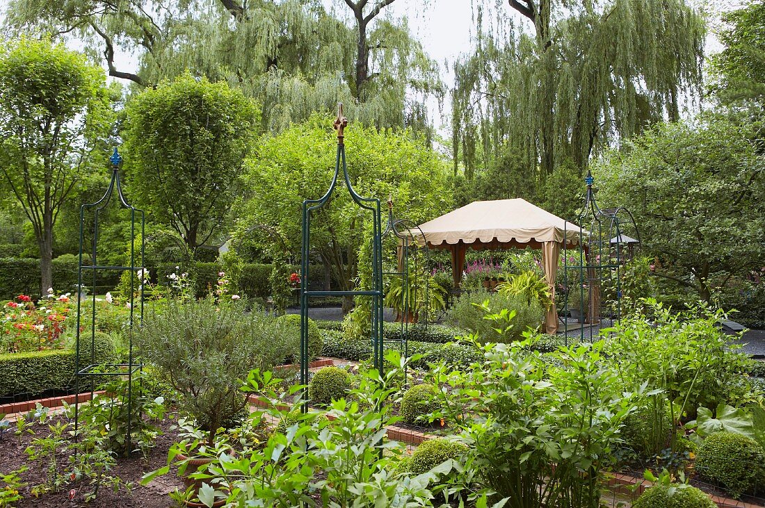 Sommerlicher Garten mit Pavillon und großen Weiden im Hintergrund