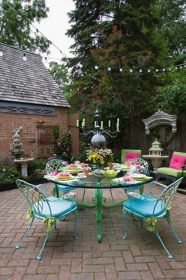 Gartenterrasse mit filigranen Gartenstühlen in Pastellblau und einem runden Glastisch mit pastellgrünem Metallfuß