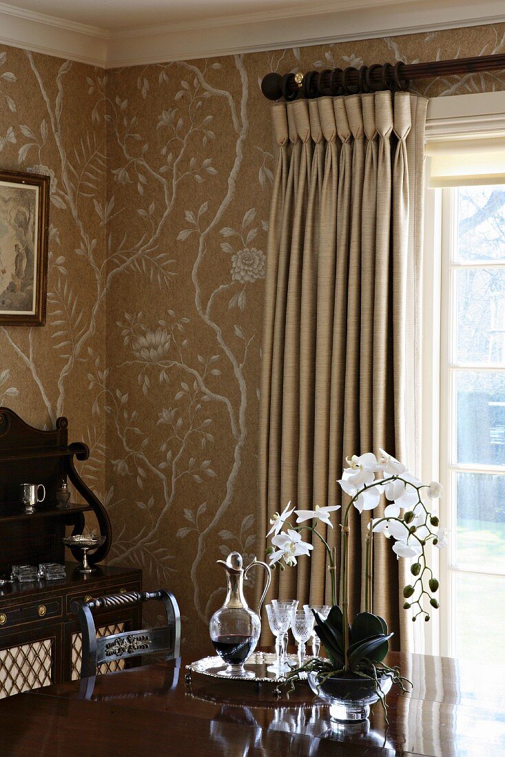 Carafe of wine and wine glasses next to orchid on table in corner of room with stencilled patterns on walls