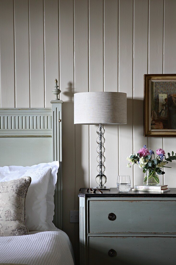 Modern table lamp on traditional bedside table next to bed against white wood panelling