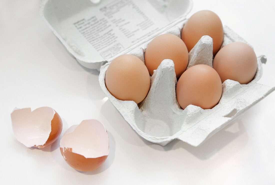 Brown eggs in an egg box with eggshells next to it