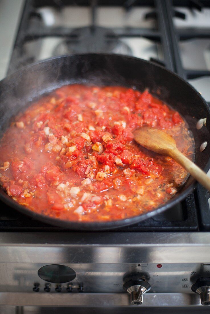 Tomatensauce mit Speck in Pfanne auf Gasherd