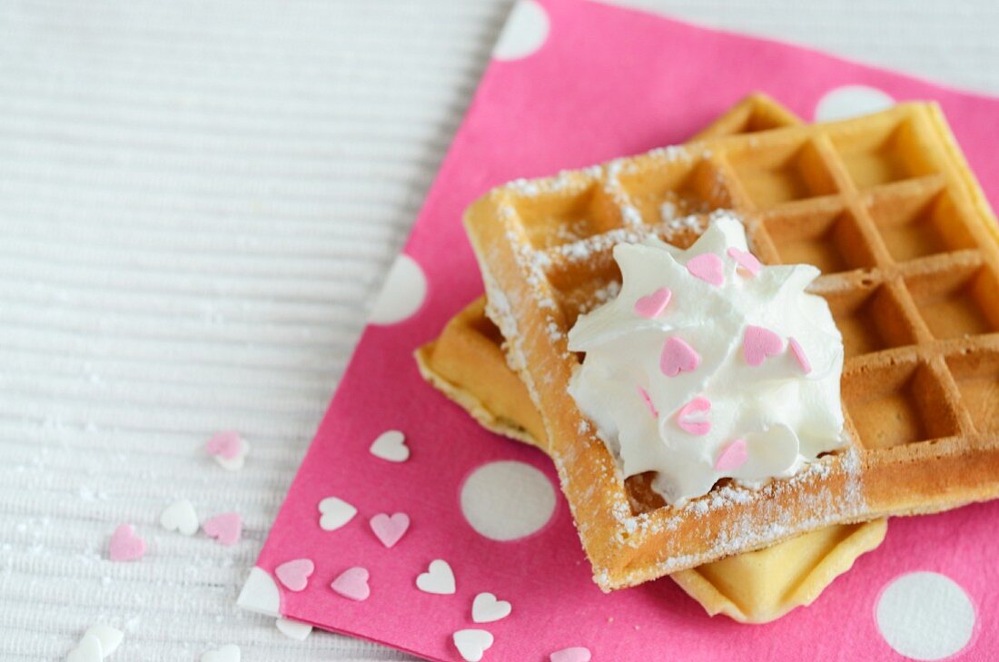 Waffles with cream and sugar hearts on a pink napkin