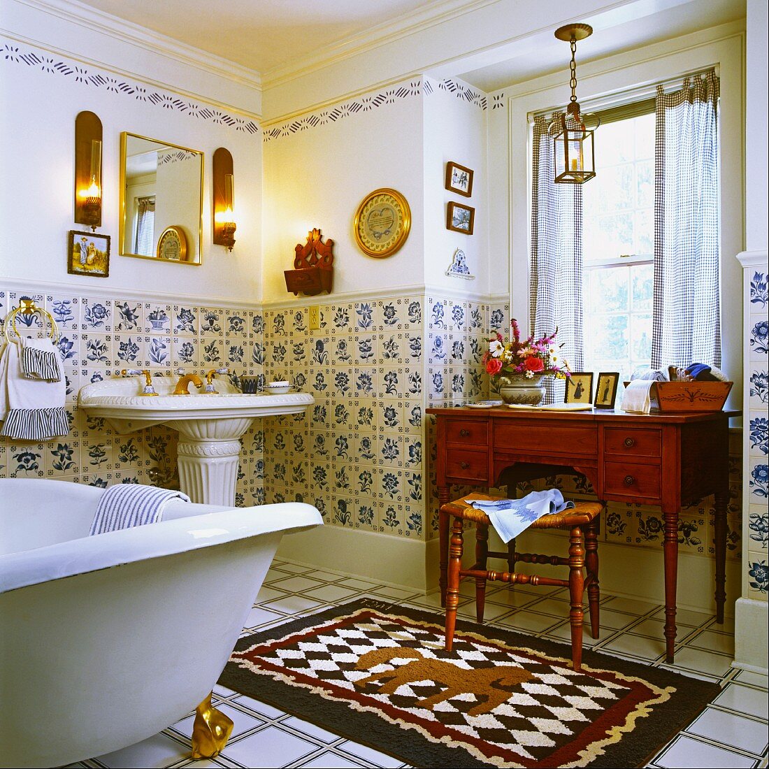Nostalgisches Badezimmer mit antikem Waschtisch, einem Standwaschbecken, einer freistehenden Badewanne mit goldenen Füssen und blau-weissen Wandfliesen