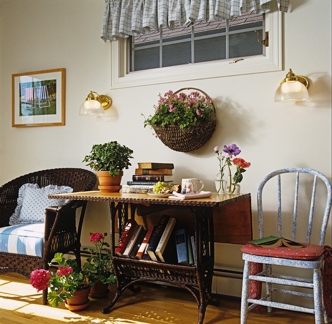 Tisch mit Büchern und Blumen, Korbsessel und Stuhl auf einer Veranda