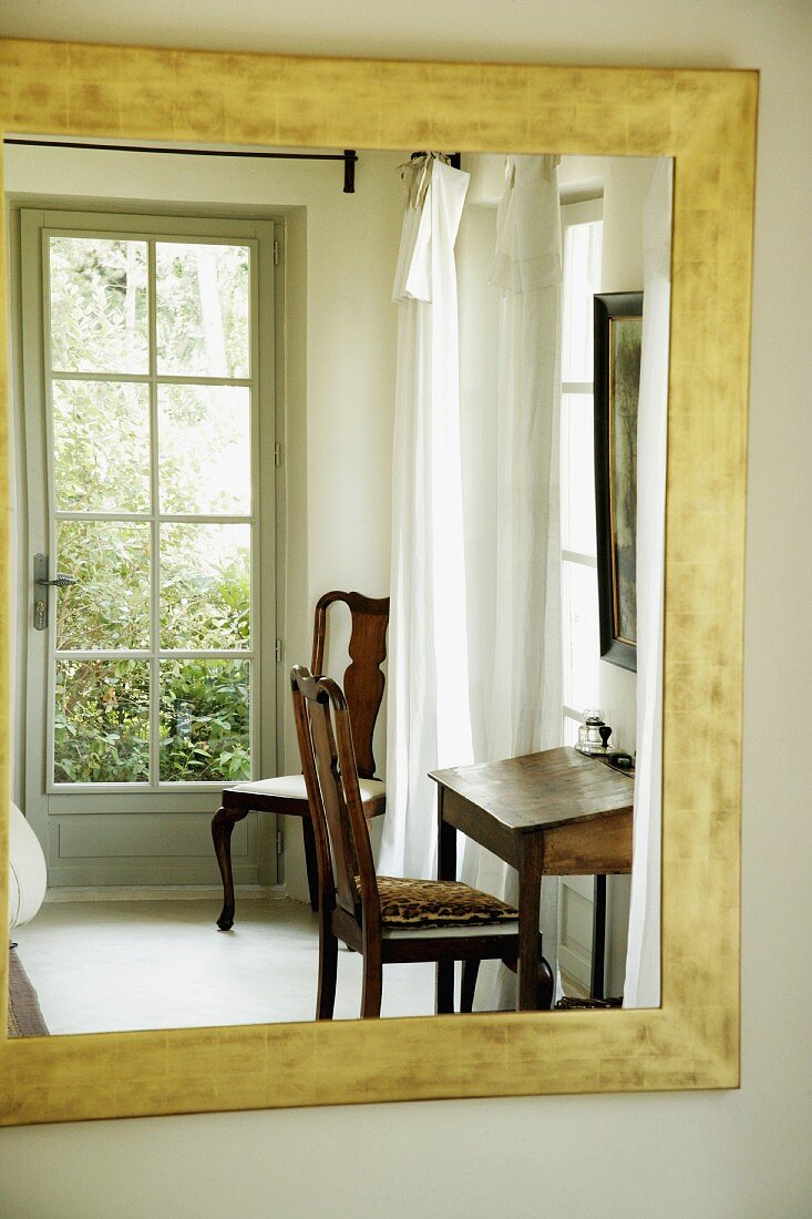 Reflection in mirror of chair at small antique desk