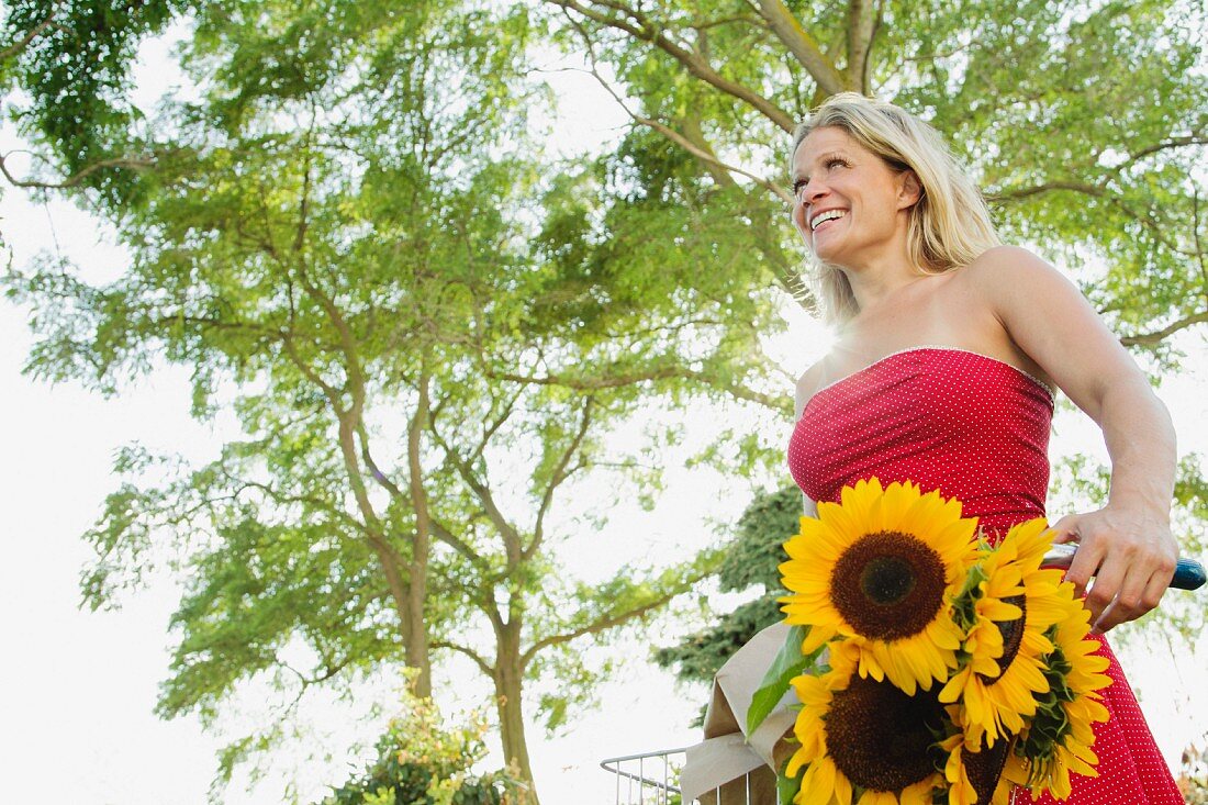 Blonde Frau mit Farhrrad und Sonnenblumen im Fahrradkorb