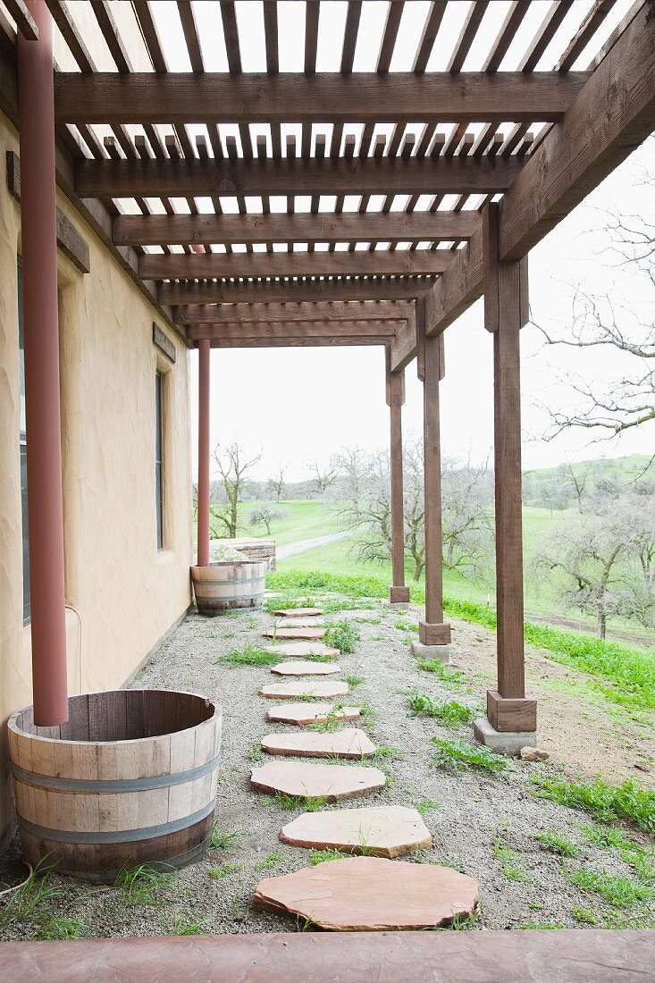 Pathway of rough stone slabs below pergola running along house with view of countryside