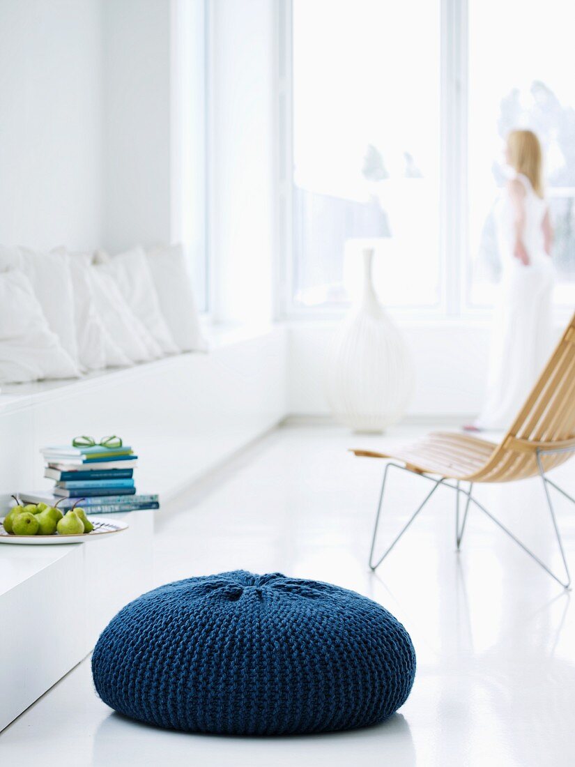 Sitzkissen mit selbstgestricktem, blauen Überzug in minimalistisch weiss gestalteter Wohnumgebung