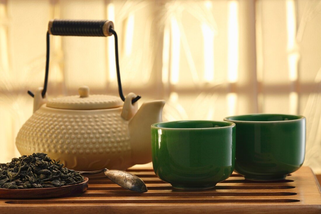 Grüne Teeblätter, Teekanne und Teestassen