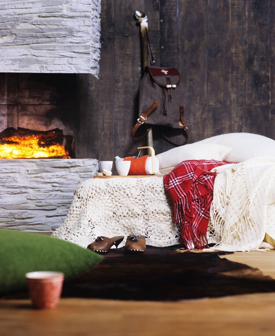 Crocheted and woollen blankets on bed next to fireplace