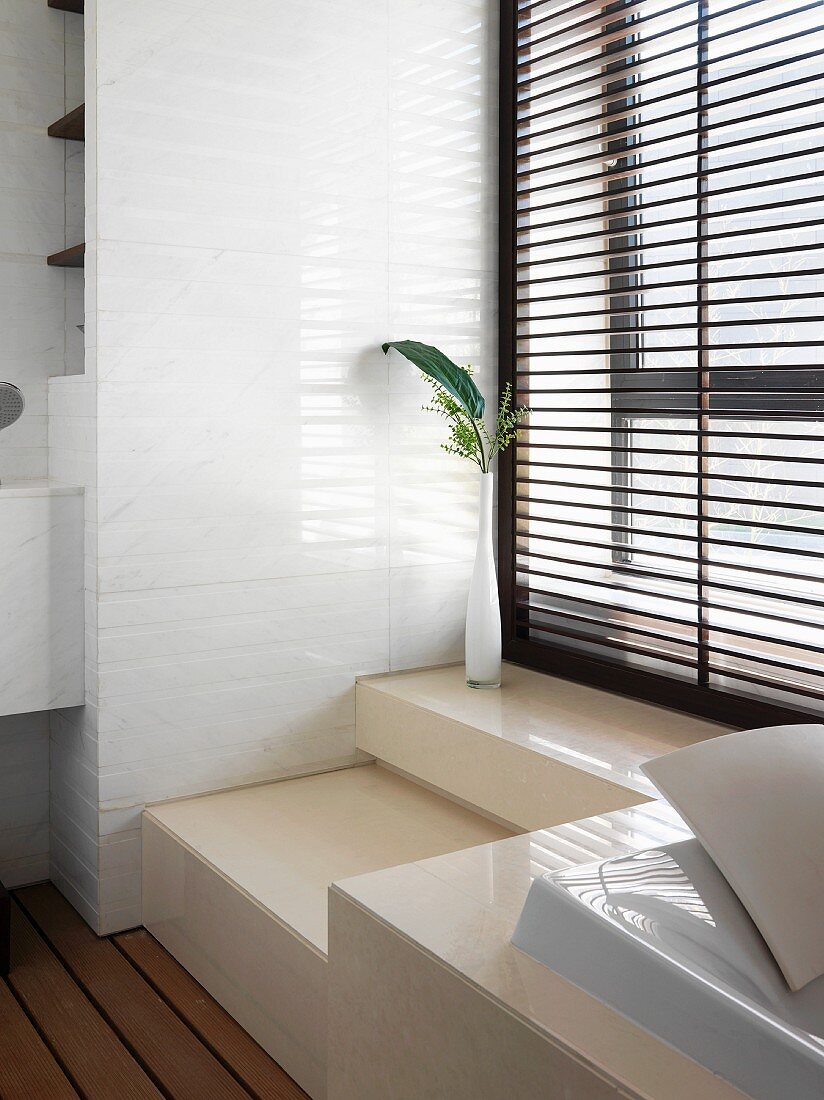 Im Podest eingebaute Badewanne vor Fenster mit geschlossener Jalousie im minimalistischen Bad